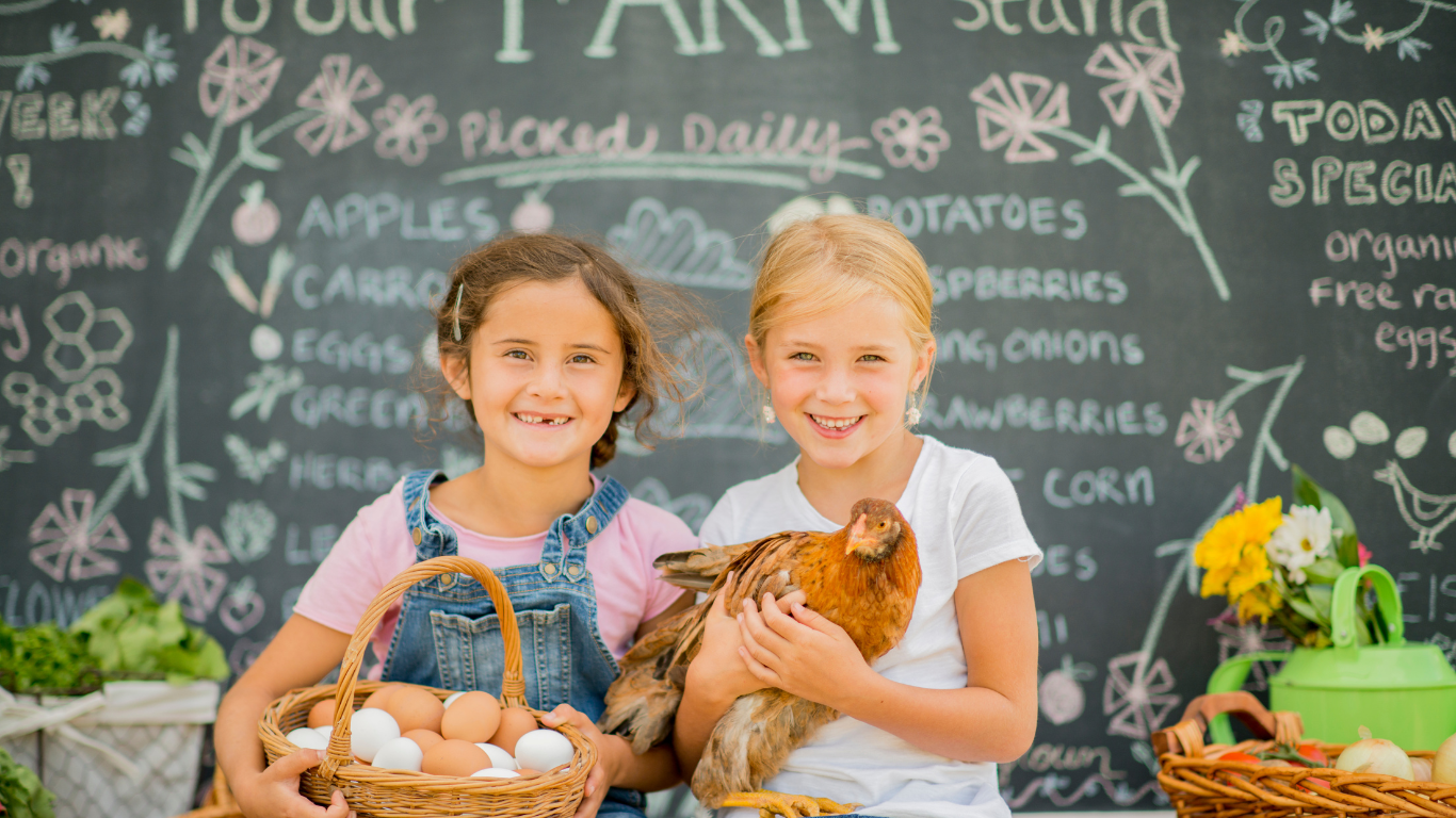 Girls with eggs and a chicken at a farmers market, chalkboard in the background