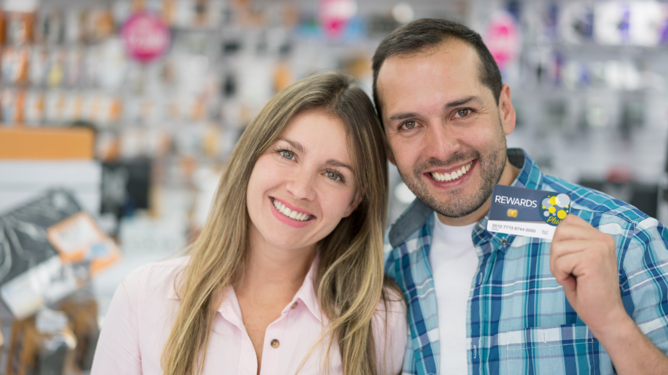 Smiling couple showing a rewards loyalty card in a store.